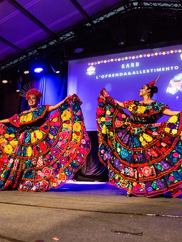 Due danzatrici con vesti tradizionali ricamate sul palco illuminato di viola, durante l'edizione 2025 del Día de los Muertos Roma.