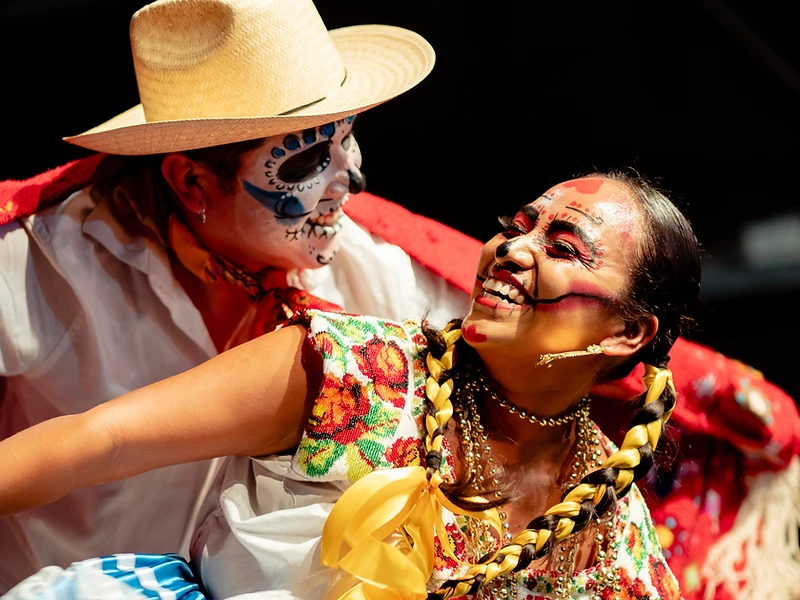 Due danzatori tradizionali messicani con trucco da Catrina e da calavera si sorridono durante una performance del Día de los Muertos Roma.