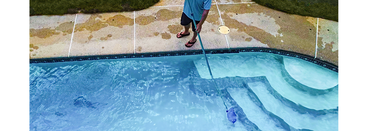 A pool tech skimming the surface of a backyard pool