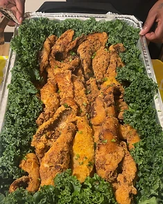 Hands holding a catering tray of golden fried fish on a bed of kale