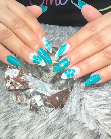 Stiletto nails with solid teal tips and white floral nail art on a clear base, posed on a crystal