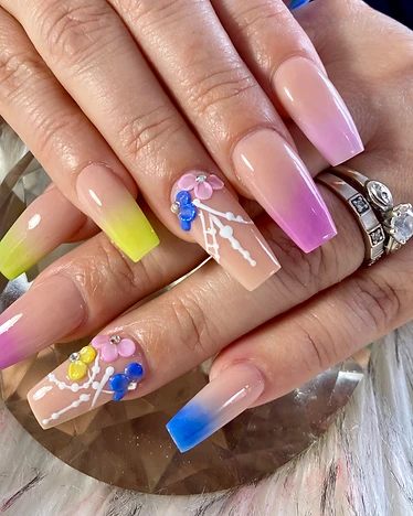 Coffin nails with pastel ombre French tips in yellow, purple, blue, and pink with 3D floral accents