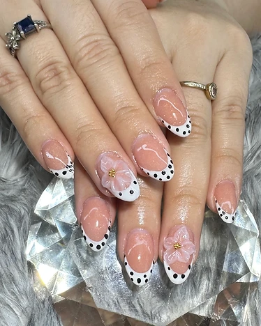 Almond nails with classic French tips, black polka dots, and 3D white floral appliques