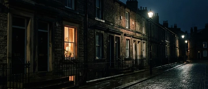 Night view of a British terraced street with one window glowing warm amber