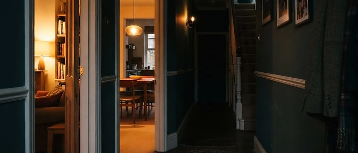 Dim British hallway with warm light spilling from two open doorways onto shadowed floorboards