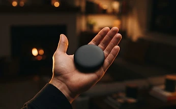 Small black streaming puck held in an open palm against a blurred dark living room