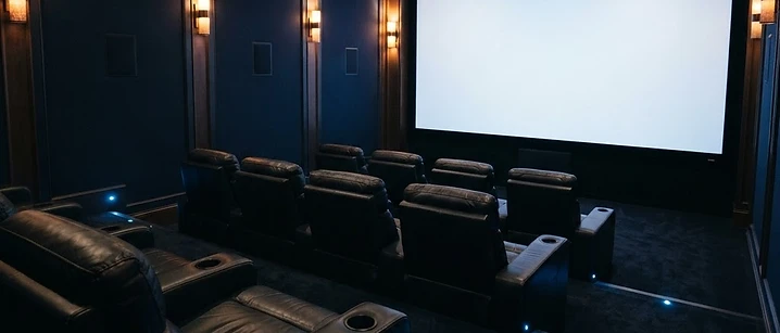 Dark home cinema with warm accent lighting and a large screen glowing softly