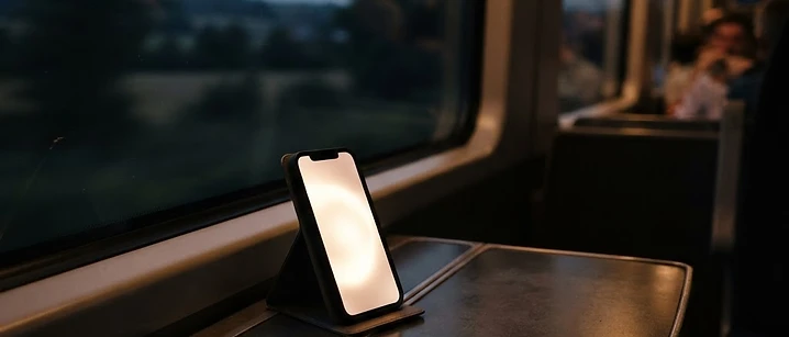 Smartphone glowing on a train tray table with dusky countryside blurred behind the window