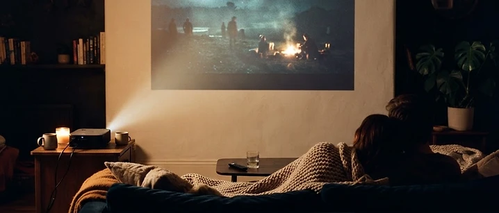 Dark living room with a small projector beaming a bright glow onto a plain wall