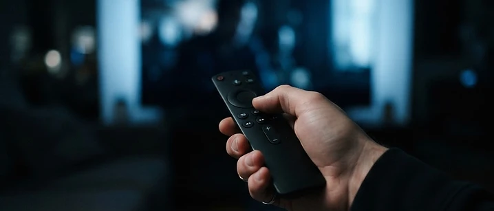 Streaming stick and remote control resting on a dark surface beside a television