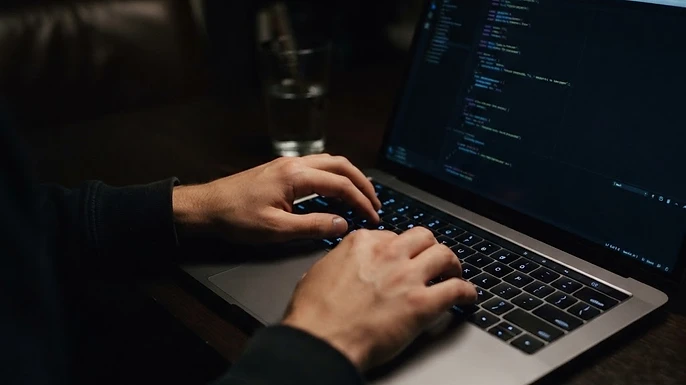 Hands typing on a laptop keyboard in a dark room, illustrating researching IPTV providers on Reddit