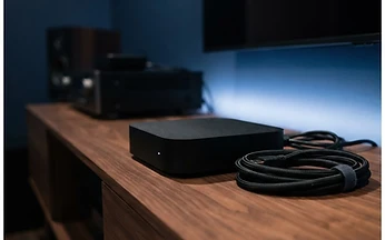 Matte black set-top streaming box on a walnut media unit with a soft blue glow behind