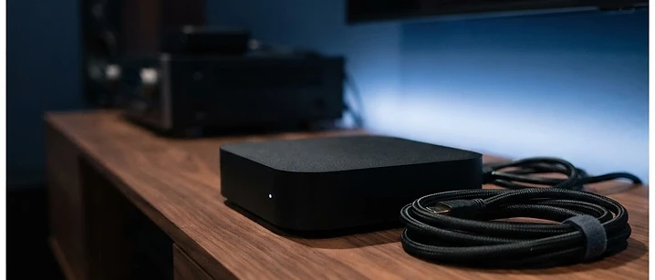Matte black set-top streaming box on a walnut media unit with a soft blue glow behind