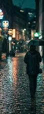 Rain-soaked British city street at night with a lone figure