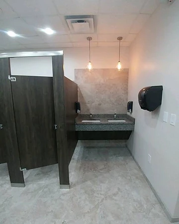 Completed commercial restroom with a double vanity, pendant lighting and wood-grain stall partitions