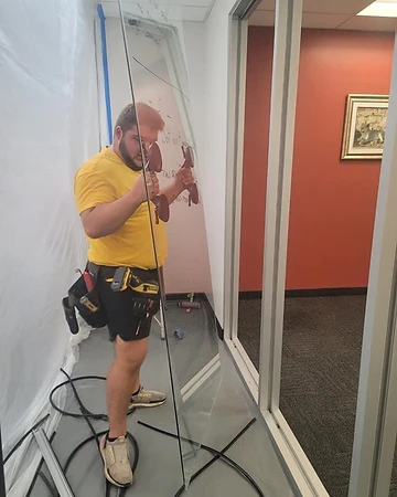 Installer setting a glass partition panel into an aluminum frame during a commercial build-out