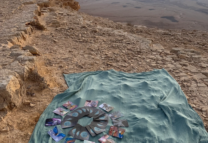 קלפי חכמת פיות הנפש פרושים במעגל על בד, מול נוף המדבר בשעת בין הערביים