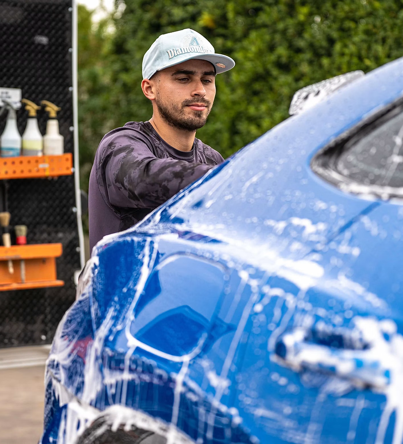 Auto detailing website design: detailer foam-washing a blue car beside a mobile detailing van