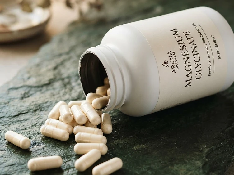Magnesium complex capsules spilling from an open MAGNOLIA bottle on dark green slate