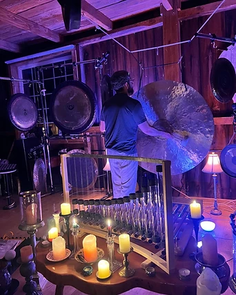 A practitioner playing a gong surrounded by candlelight