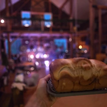 A hand holding a freshly baked loaf of bread in a baking pan