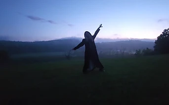A figure with arms outstretched against a misty hillside at dusk