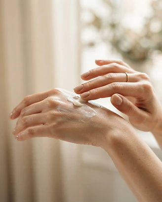 Hands gently applying a creamy moisturizer to the back of the hand in soft window light
