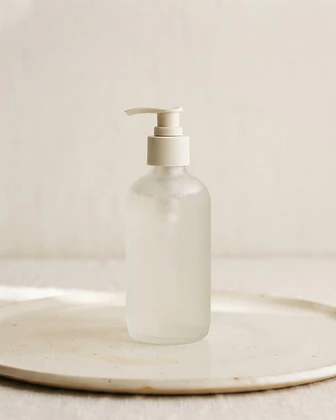 Frosted glass pump bottle of Longevity Cleanser on a porcelain surface in soft light