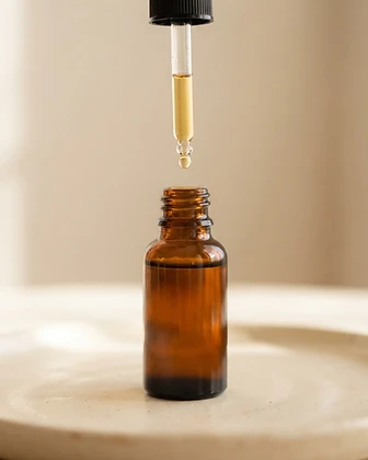 Amber glass dropper bottle of Peptide Serum with a golden droplet suspended from the dropper