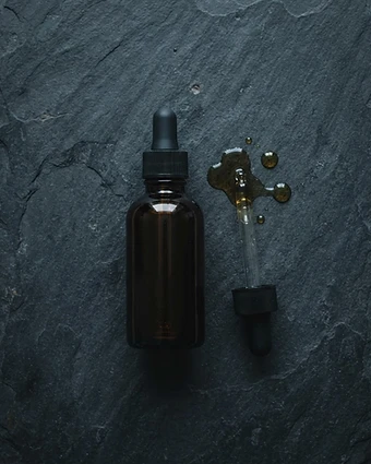 Amber glass night treatment bottle with dropper on dark stone under soft moody light