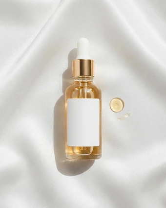 Clear glass dropper bottle of golden serum on white satin with a single droplet beside it