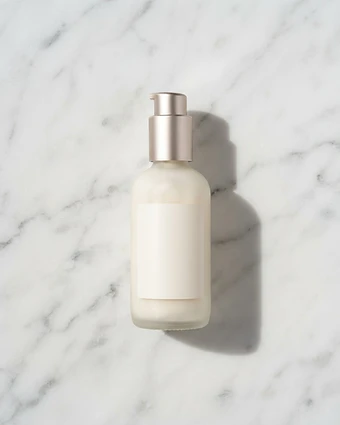 Frosted glass cleanser pump bottle with champagne cap on white marble, photographed from above