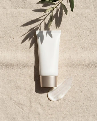 Matte white sunscreen tube with champagne cap and a smear of mineral lotion on ivory linen in sunlight