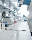 Glass pipette dispensing clear liquid into a laboratory beaker