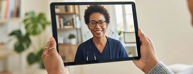A patient holding a tablet during a video visit with a physician in a bright office