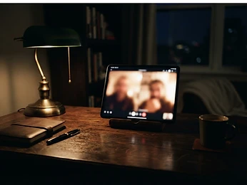 A tablet on an oak desk showing a video call