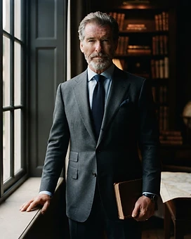 A composed man in a tailored suit standing by a tall window