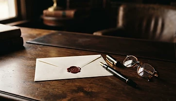 A desk with an envelope, fountain pen, and reading glasses