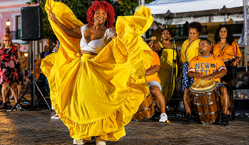 A dancer in a yellow skirt with drummers playing behind her at dusk