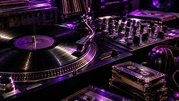 Vinyl record, turntable, mixer and cassette tapes in purple studio light.