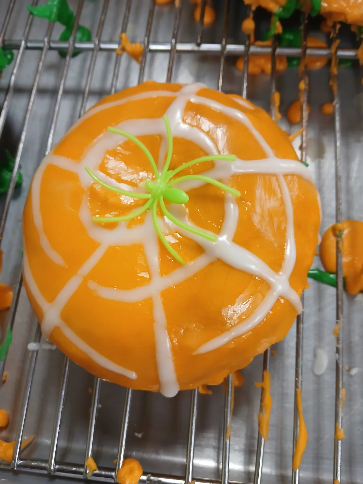 An orange donut iced with a white spiderweb and a green spider