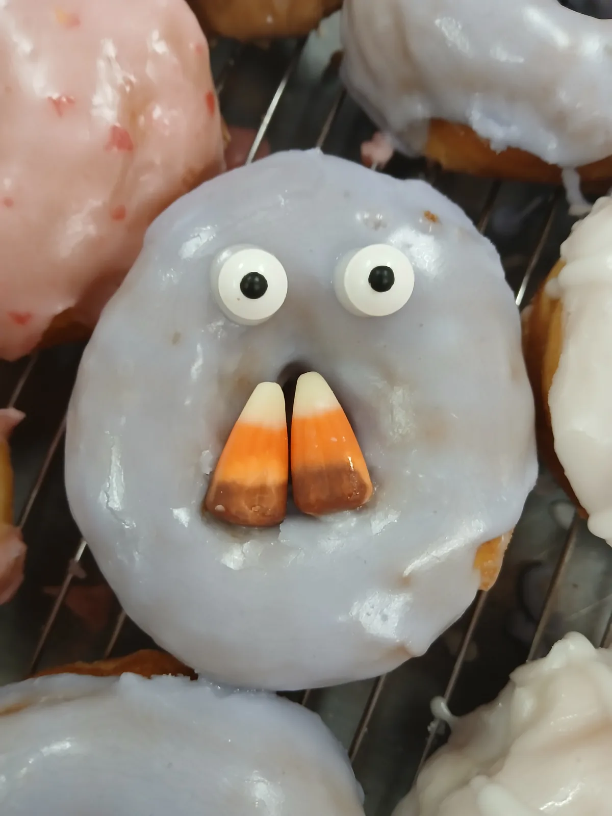 A ghost donut with candy eyes and candy corn teeth