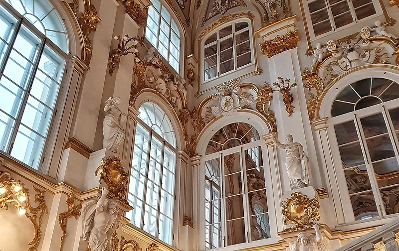 A grand rococo staircase hall with gold-leaf mouldings, arched windows and classical statuary