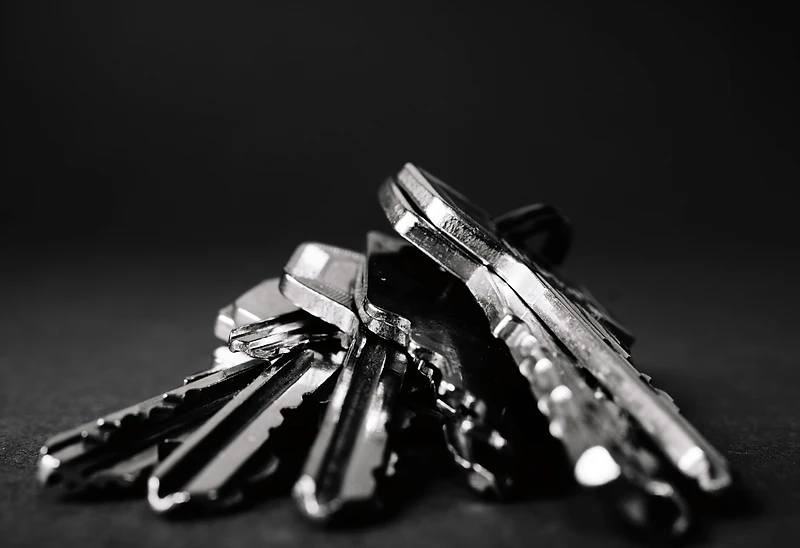 A pile of metal keys resting in deep shadow, one key sharp in the light
