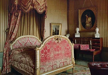 Gilded state bed in red damask beneath cherub-topped canopy