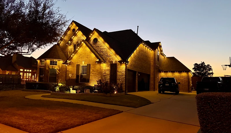Wide twilight view of a luxury home illuminated with warm white architectural lighting