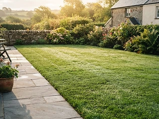 Woman crouching on a patio, touching the edge of a neatly mowed lawn in a garden.