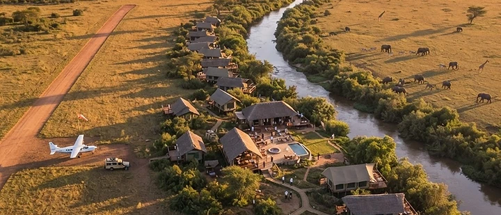 Aerial view of a safari tented camp beside a river in the Kenyan bush at sunrise