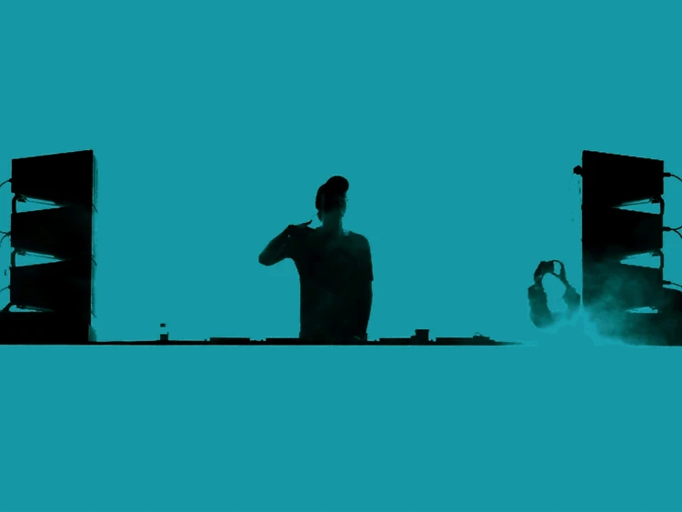 Silhouette of a DJ behind the decks against a bright teal stage backdrop