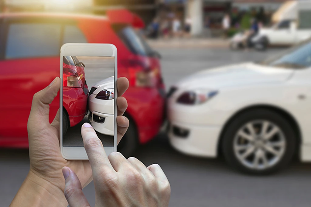 A person photographing two damaged cars with a smartphone.